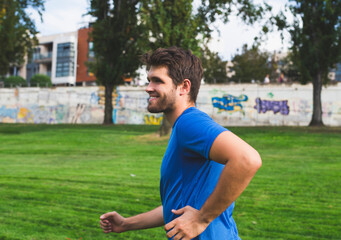 Bearded man dressed in sportswear smiles as he runs through the park.