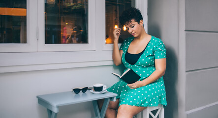 Thoughtful woman looking at book at table with cup and sunglasses in outside cafe