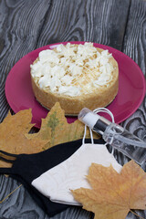 Cheesecake with white chocolate. Nearby are medical masks, antiseptic and dried maple leaves. On pine planks painted black and white.