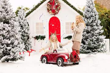 Two blonde girls blow up a candy flapper near snow white Christmas house