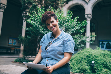Portrait of happy Hispanic digital nomad holding modern digital tablet and smiling at camera during...