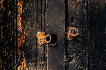 Rusty eye bolts attached to a burned wooden door lit by the evening sun