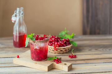 Glass of red currant cocktail or mocktail, refreshing summer drink with crushed ice and sparkling water on a wooden background.