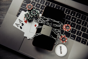 Smartphone and padlock, poker chips and playing cards on laptop keyboard. Concept of Law and regulation of gambling.