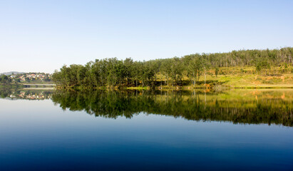 a dam with trees on the horizon reflecting in the water making a green and blue contrast