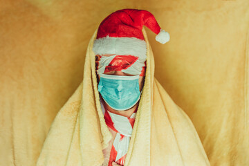 man with santa claus hat with blue hygienic mask, with yellow blanket and eyes covered with a prohibition bandage