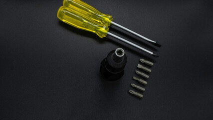 Yellow screwdriver and small multi-bit screwdriver on a black background