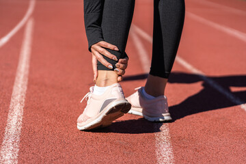 Fototapeta na wymiar Close up of athletic woman runner touching foot in pain due to sprained ankle, rear view. Running sport, injury from workout