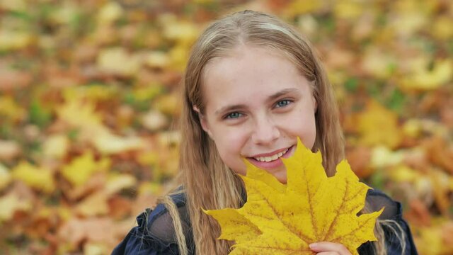 A young girl of 13 years old with autumn leaves poses in front of a video camera.