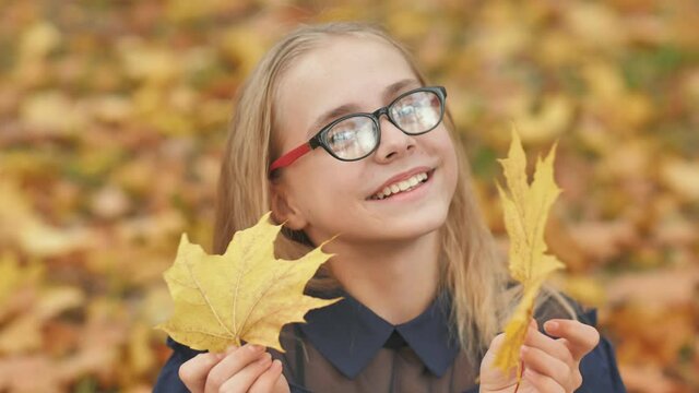 A young girl of 13 years old with autumn leaves poses in front of a video camera.