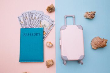 Pink sunitcase and passport with money on blue pink background with shells. Travel, summer vacation or tourism concept.