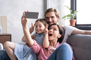 Cheerful family with children laughing taking selfie together on phone, young mom holding...