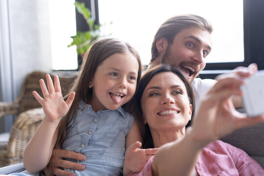 Cheerful family with children laughing taking selfie together on phone, young mom holding smartphone making photo of daughter at home, loving parents having fun with adopted kids and gadget