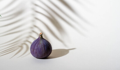 Purple figs on a beige background, shadow from a palm tree