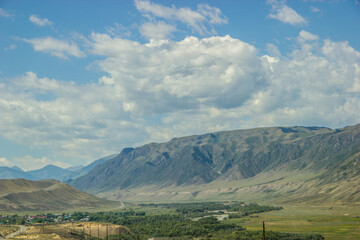 Landscape of Central Asian rural area in August. Mountains, hills, cloudy blue sky and a small distant village.