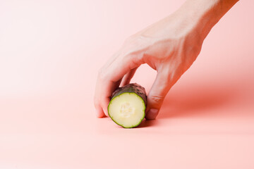 picking up a cut cucumber with a man's hand on a pink studio background