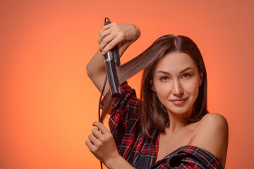 Portrait of a beautiful brunette woman with a hair straightener on an orange background....