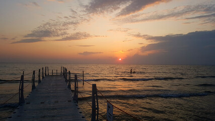 Small sea pier at sunset.
Pink sunset in the clouds, small sea waves on a warm summer evening.