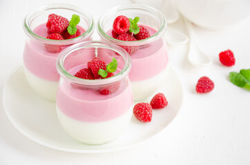 Raspberry yogurt panna cotta or mousse with fresh raspberries on top in jars on a light background....