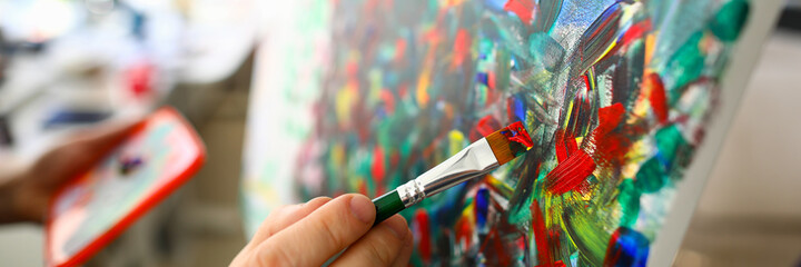 Close-up view of persons hand painting on canvas using paintbrush with red colour. Abstract artwork. Fragment of masterpiece. Creative hobby and art concept