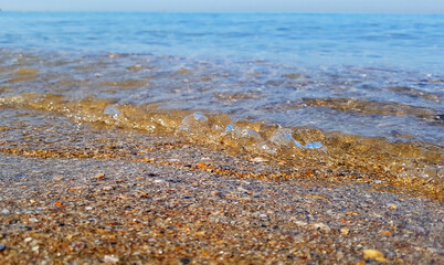 Fototapeta na wymiar Seashore during calm/Берег моря в штильThe clear sea, when calm, pacifies on a beautiful summer day. Sand with small shells shimmer in the light of bright sunlight.