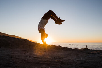 male athlete balancing on his hands at sunrise