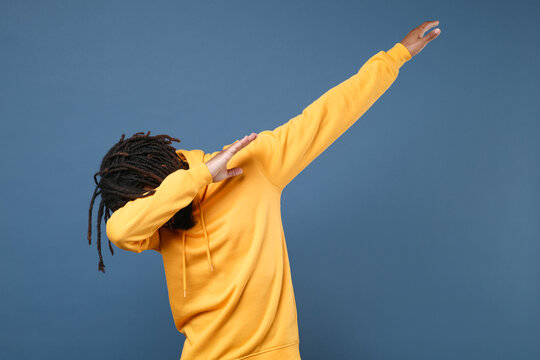 Young african american man guy wearing yellow streetwear hoodie posing isolated on blue wall background studio portrait. People sincere emotions lifestyle concept. Showing DAB dance gesture.