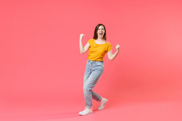 Fototapeta na wymiar Full length portrait of happy screaming young brunette woman 20s wearing yellow casual t-shirt posing standing clenching fists doing winner gesture isolated on pink color wall background studio.
