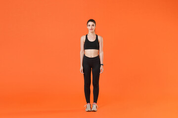 Fototapeta na wymiar Full length portrait of beautiful attractive strong young fitness sporty woman in black sportswear posing training working out standing looking camera isolated on orange color wall background studio.