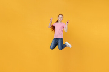 Fototapeta na wymiar Full length children studio portrait of smiling little ginger redhead kid girl 12-13 years old in pink casual t-shirt posing jumping showing victory sign isolated on bright yellow color background.
