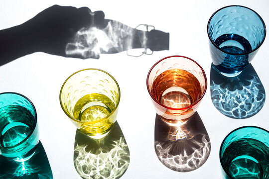 Shadow of hand holding bottle pouring water in colorful glasses