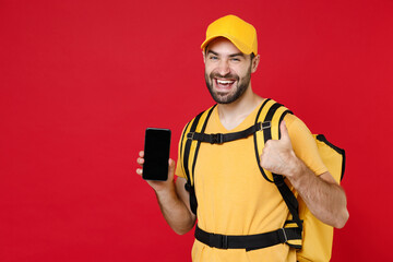 Delivery man in yellow cap t-shirt uniform thermal bag backpack with food hold cellphone isolated on red background studio Guy male employee work as courier Service coronavirus covid-19 virus concept