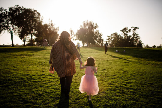 Aunt and niece holding hands walking in park at sunset