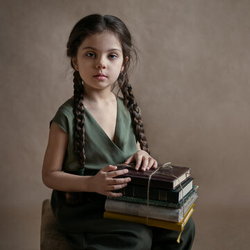 a girl with long pigtails sits and holds a stack of books in her lap