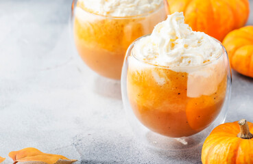 Pumpkin spiced latte or coffee in double glass cup on gray table. Autumn or winter hot drink in festive table setting
