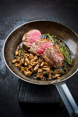 Fried dry aged beef fillet steak natural with king trumpet mushroom and herbs offered as close-up in a rustic frying pan
