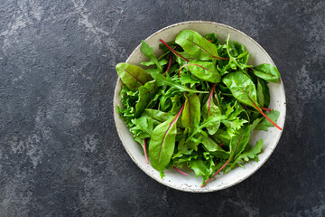 Mixed salad leaves in a bowl on a dark gray stone table, top view