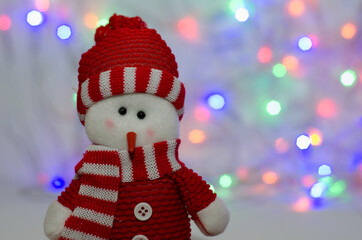 toy decorative Christmas snowman on a background of lights in a red hat and scarf
