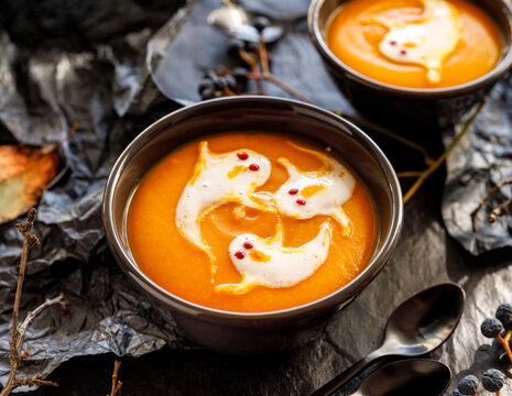 Halloween pumpkin soup decorated with cream ghosts in a black bowl close up view