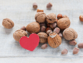 Engagement ring among nuts and a paper heart on white background