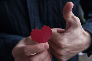 Obraz premium A man holding in one hand a cardboard heart, the other hand makes the sign 