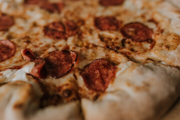 A large round juicy mouth-watering pizza with cheese and salami lies on a cardboard box from a delivery package. paper backing. close view. see flour. good thin dough