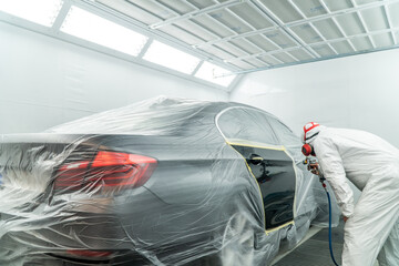 Automobile painting. Car painter with gun in chamber. Spray operation. 