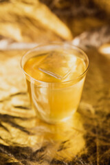 A bright yellow cocktail with ice in a rocks lowball glass