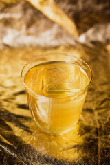 A bright yellow cocktail with ice in a rocks lowball glass