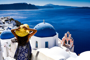 Woman with sun hat and blue dress in front of beautiful traditional Santorini church and the deep...