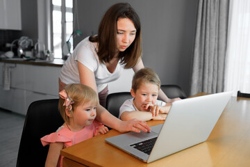 A mother with a young son and daughter watching educational programs on a laptop.