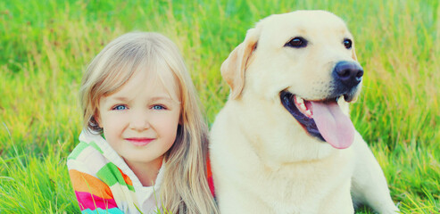 Portrait little girl child and labrador retriever dog together on the grass in summer park