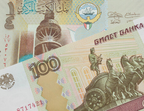 A macro image of a Russian one hundred ruble note paired up with a colorful, plastic quarter dinar from Kuwait.  Shot close up in macro.