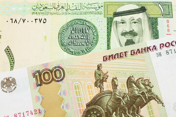 A macro image of a Russian one hundred ruble note paired up with a green and yellow one riyal bank...